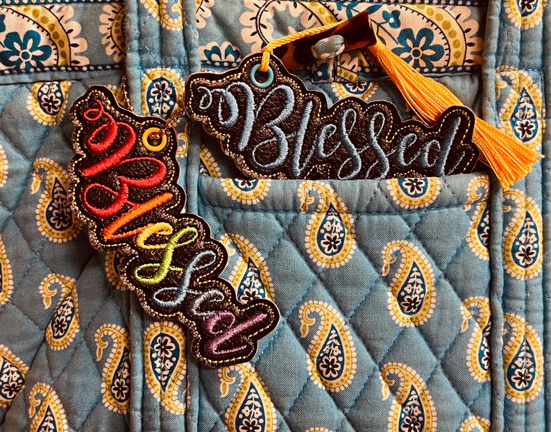 Puede incluir: Dos parches de tela con las palabras "Blessed" y "Wild Soul" bordadas en hilo de colores. Los parches est&aacute;n unidos a una tela acolchada azul con un patr&oacute;n de cachemira.