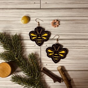 May include: A pair of black and gold bee earrings. The bees are embroidered with yellow thread and have black wings.