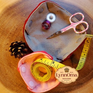 May include: A pink and red felt sewing kit with a yellow tape measure, pinking shears, and spools of thread. The kit has a label that reads "Lynnoma Designs Est. 2016".