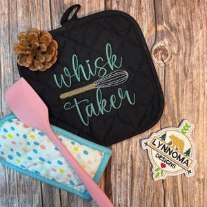 May include: A black quilted pot holder with the words "whisk taker" embroidered in teal, a pink spatula, and a small, colorful patterned trivet. A pinecone and a "Lynnomadesigns" patch are also present.