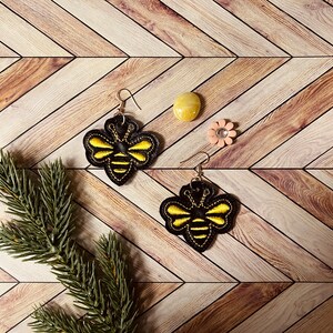 May include: A pair of black and yellow bee-shaped earrings with a woodgrain background.