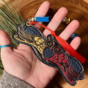 May include: A black leather bookmark with colorful embroidered bird design. The bookmark has a red and blue tassel.