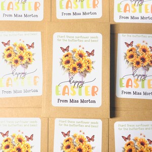 May include: A set of six brown paper seed packets with colourful labels. Each label features a sunflower bouquet with butterflies and the text "happy easter" in a colourful font. The text "From Miss Morton" is printed below the greeting.
