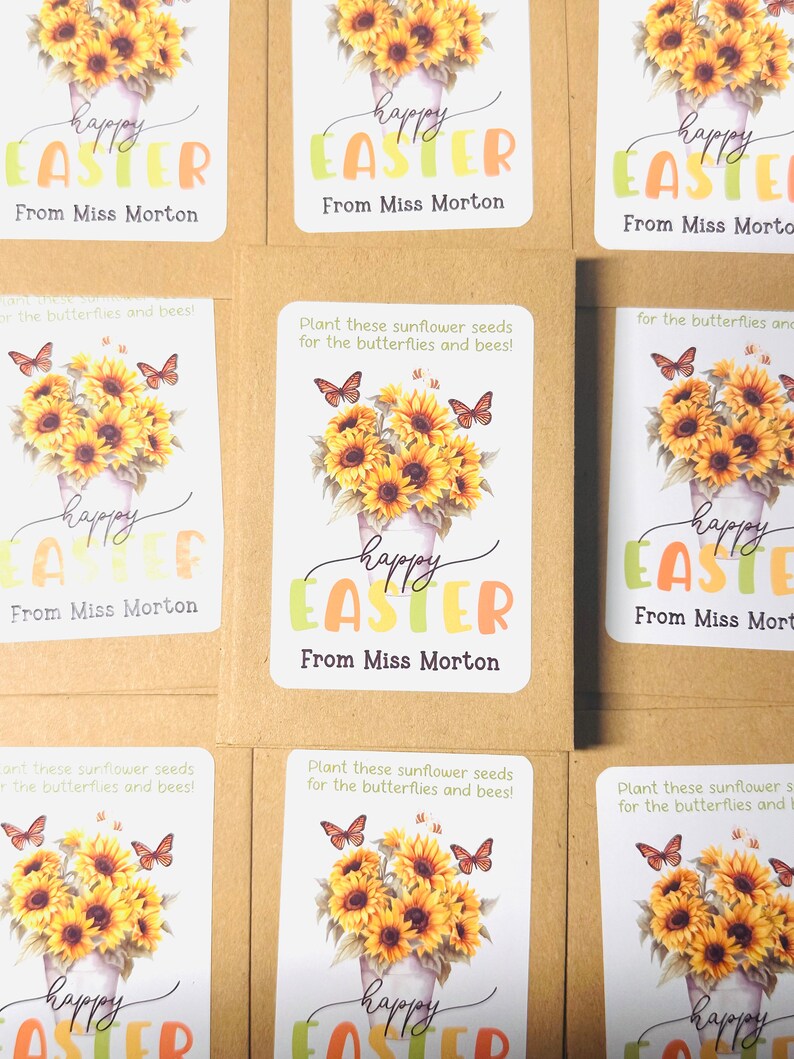 May include: A set of six brown paper seed packets with colourful labels. Each label features a sunflower bouquet with butterflies and the text "happy easter" in a colourful font. The text "From Miss Morton" is printed below the greeting.