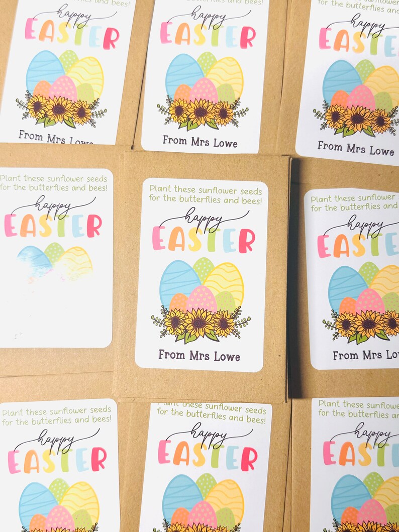 May include: Six brown paper bags with white labels. Each label features a colourful illustration of Easter eggs with sunflowers and the text "Happy Easter" and "From Mrs Lowe". The labels also include the text "Plant these sunflower seeds for the butterflies and bees!"