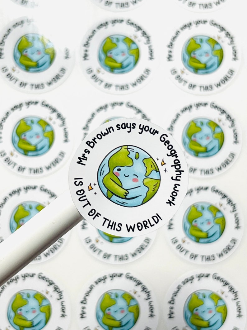 May include: Round white stickers with a green and blue cartoon earth hugging itself. The text on the sticker says "Mrs. Brown says your Geography work is out of this world!"