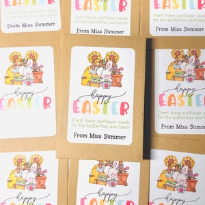 May include: A set of six colourful Happy Easter seed packets featuring a bunny rabbit holding a watering can and surrounded by flowers and gardening tools. The packets have a white background with a colourful Happy Easter message and the text "Plant these sunflower seeds for the butterflies and bees! From Miss Summer."