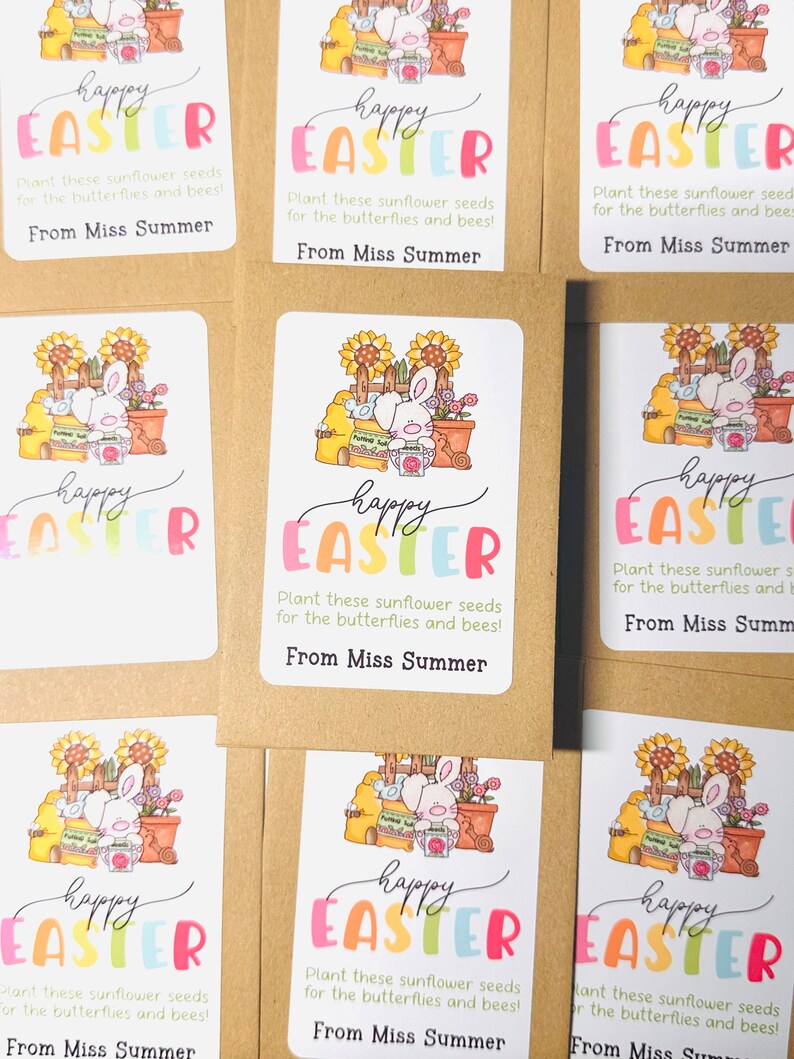 May include: A set of six colourful Happy Easter seed packets featuring a bunny rabbit holding a watering can and surrounded by flowers and gardening tools. The packets have a white background with a colourful Happy Easter message and the text "Plant these sunflower seeds for the butterflies and bees! From Miss Summer."
