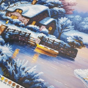 May include: A winter scene with a small cottage covered in snow, a wooden bridge over a frozen lake, and trees covered in snow. The sky is a light blue with a hint of pink.