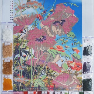 May include: A close-up of a diamond painting kit with a colorful floral design featuring red poppies. The kit includes a canvas, beads, and instructions. The beads are organized in small plastic bags labeled with numbers.