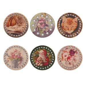 Op de afbeelding: Zes ronde houten breinaalden met verschillende ontwerpen. De ontwerpen omvatten een kat, bloemen, de kerstman en een kat. De breinaalden hebben een diameter van ongeveer 20 cm.