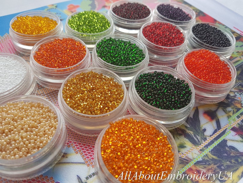 May include: Assortment of small, round, colorful beads in clear containers. The beads are arranged in rows and are various colors, including white, green, orange, red, and black.