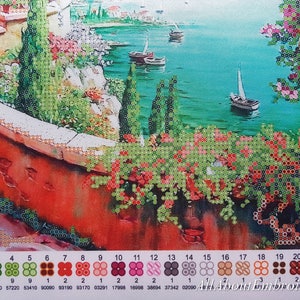 Puede incluir: Un kit de pintura de diamantes colorido que presenta una escena costera con una pared de ladrillo rojo, arbustos verdes y veleros en la distancia. El kit incluye una variedad de colores, incluyendo rojo, verde, azul y marr&oacute;n.