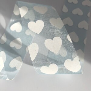 May include: Light blue ribbon with a white heart pattern. The ribbon is sheer and has a subtle shimmer.