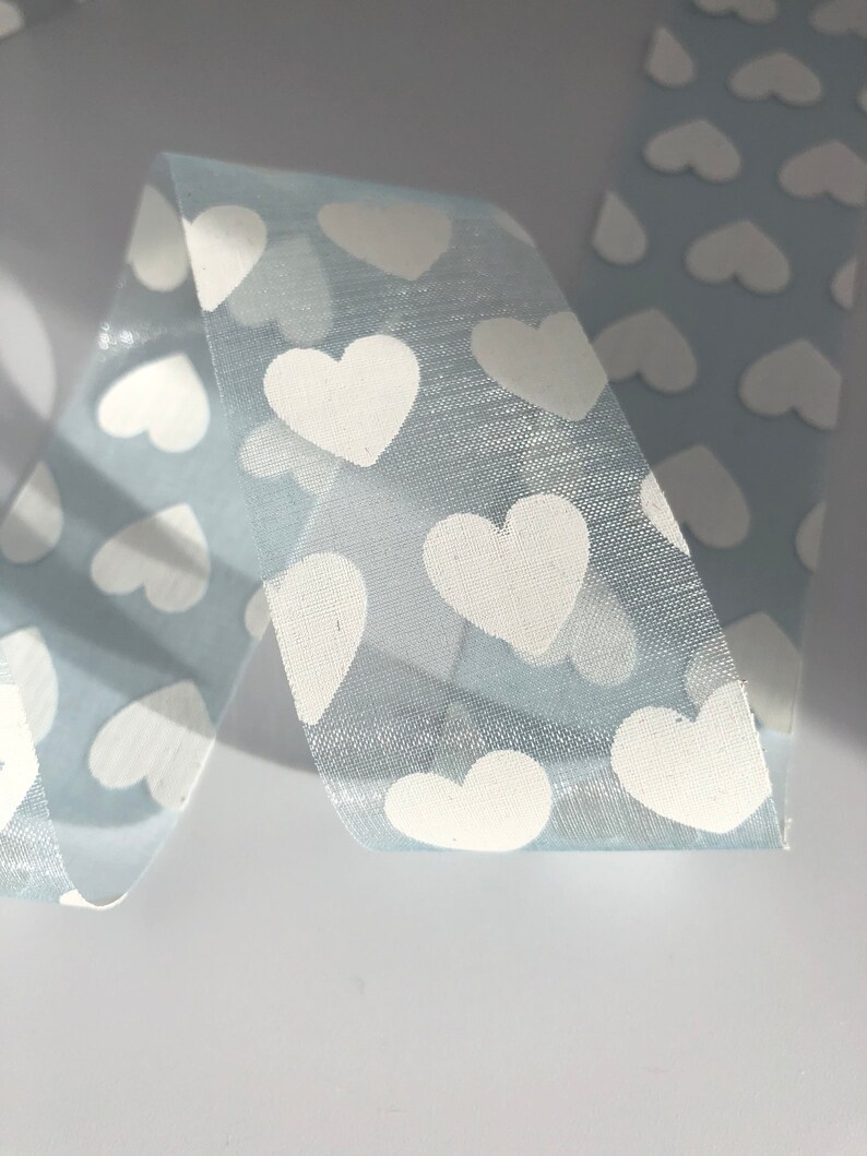 May include: Light blue ribbon with a white heart pattern. The ribbon is sheer and has a subtle shimmer.
