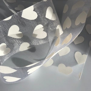 May include: Gray sheer ribbon with white heart-shaped patterns. The ribbon is folded and overlapping.