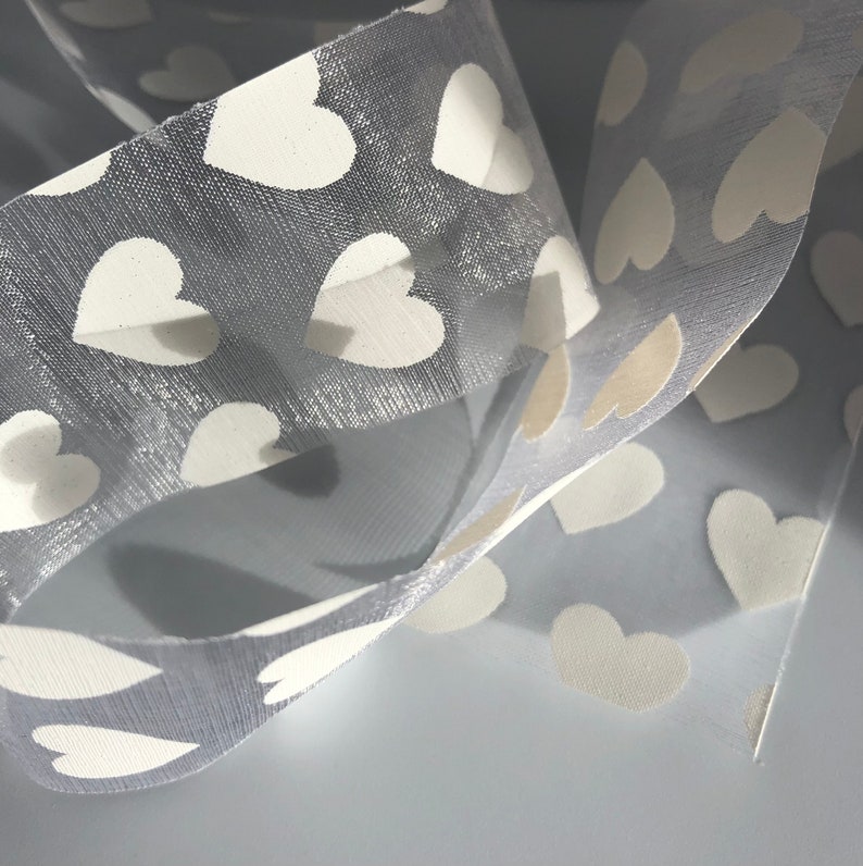 May include: Gray sheer ribbon with white heart-shaped patterns. The ribbon is folded and overlapping.