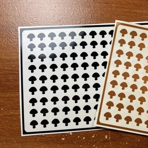 May include: Two sheets of sticker paper with a repeating pattern of black and gold mushroom silhouettes.