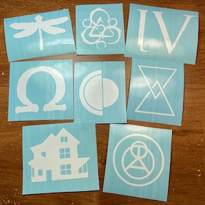 May include: Eight square light blue vinyl decals featuring white die-cut designs. The graphics include a dragonfly, a circular emblem, the Roman numeral IV, an omega symbol, a crescent moon shape, a geometric triangle, a house, and a circular logo.