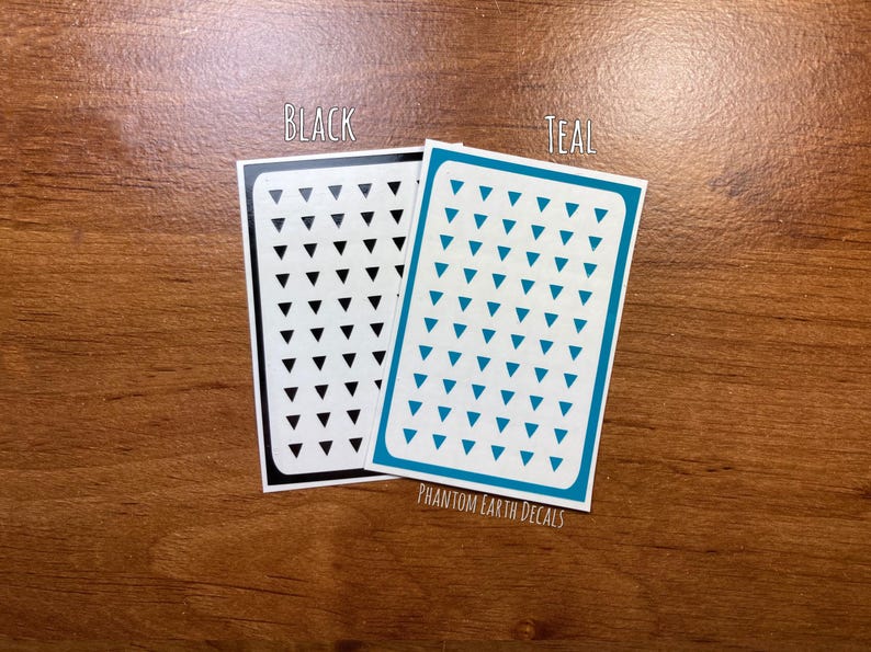 Pu&ograve; includere: Due fogli di carta adesiva con un motivo a triangolo. Un foglio &egrave; nero con triangoli neri e l'altro foglio &egrave; turchese con triangoli turchesi. Il testo "BLACK" e "TEAL" &egrave; stampato sopra ogni foglio. Il testo "PHANTOM EARTH DECALS" &egrave; stampato sotto i fogli.