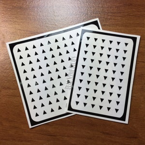 Pu&ograve; includere: Due fogli di adesivi neri e bianchi con un motivo ripetitivo di piccoli triangoli neri su sfondo bianco. I fogli di adesivi sono etichettati "Dead Scene Decals".