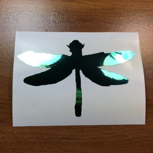 May include: A green iridescent dragonfly silhouette vinyl decal. The decal is on a white background.