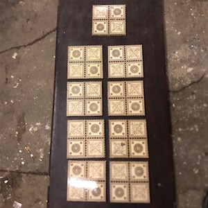 May include: A set of 10 cream-coloured ceramic tiles with a brown floral pattern. The tiles are arranged in a grid pattern on a dark brown surface.