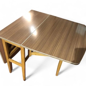 May include: A brown folding table with a wood grain pattern and a light brown trim. The table has a simple design with four legs and a rectangular top.
