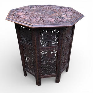 May include: An intricately carved, dark brown octagonal table. The tabletop and sides feature detailed floral patterns. The table has an openwork design and stands on short legs. The wood has a rich, warm tone, and the style is ornate and decorative.