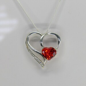 May include: A silver necklace with a double heart pendant. The pendant features a large red heart-shaped gemstone in the center.