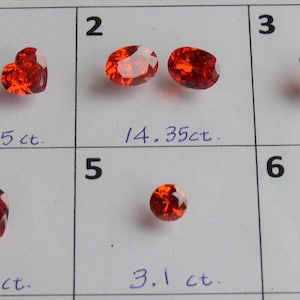 Może przedstawiać: Sześć czerwonych kamieni szlachetnych o różnych kształtach i rozmiarach, oznaczonych numerami od 1 do 6 i podanych wagach w karatach. Kamienie szlachetne są prezentowane na białym tle.