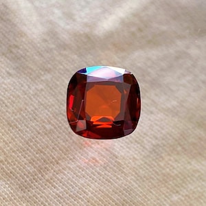 Może przedstawiać: Czerwony, poduszkowaty kamień szlachetny o lekko zaokrąglonym kształcie.