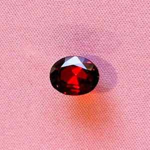 Może przedstawiać: Czerwony kamień szlachetny o fasetowym szlifie, na tle różowego materiału.