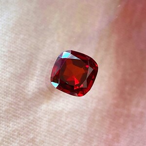 Może przedstawiać: Czerwony kamień szlachetny o szlifie poduszkowym. Kamień szlachetny jest fasetowany i ma wysoki połysk.