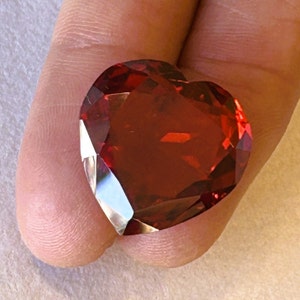 May include: A large, heart-shaped, red gemstone with a faceted cut.