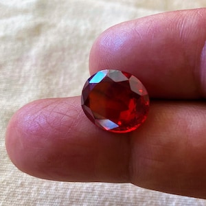Może przedstawiać: Owalny, ciemnoczerwony kamień szlachetny o szlifie fasetowym.