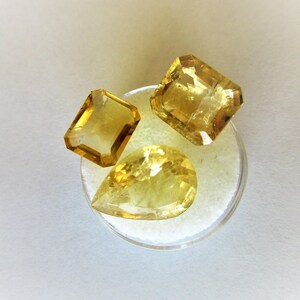 May include: Three yellow gemstones on a white background. The gemstones are cut into different shapes, including a pear, a square, and a rectangle.
