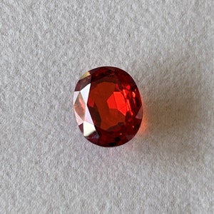 Może przedstawiać: Czerwony, błyszczący kamień szlachetny o fasetowanym szlifie. Kamień jest okrągły i ma błyszczące, wypolerowane wykończenie.