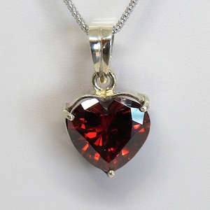 May include: A silver heart-shaped pendant necklace with a large, red, faceted gemstone.
