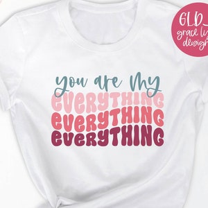 Peut inclure: Un t-shirt blanc avec le texte "you are my EVERYTHING" dans un design dégradé arc-en-ciel. Le texte est dans un style de police rétro.