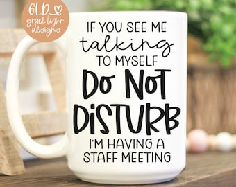May include: A white ceramic mug featuring black text that reads: IF YOU SEE ME talking TO MYSELF Do Not DISTURB I'M HAVING A STAFF MEETING. The mug has a curved handle on the left side and a smooth, cylindrical body with a flat base.