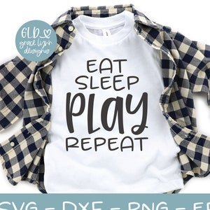 May include: White t-shirt with black text that reads "Eat Sleep Play Repeat". The shirt is folded and displayed on a plaid shirt and a pair of teal sneakers.