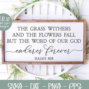 Puede incluir: Un letrero de madera con el texto "The grass withers and the flowers fall but the word of our God endures forever. Isaiah 40:8". El letrero está sobre un fondo de madera blanca con plantas verdes.