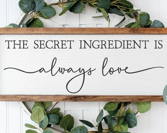 May include: A wooden sign with the text "THE SECRET INGREDIENT IS always love" in black script font. The sign is surrounded by a wreath of green leaves. The text "GLD grace lighn desigho" is in the lower right corner of the image.