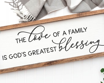 May include: A wooden sign with a white background and brown frame. The sign reads "The love of a family is God's greatest blessing".