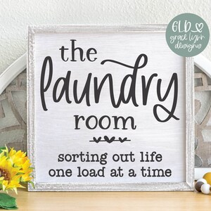 May include: White wooden sign with black text that reads "the laundry room sorting out life one load at a time".