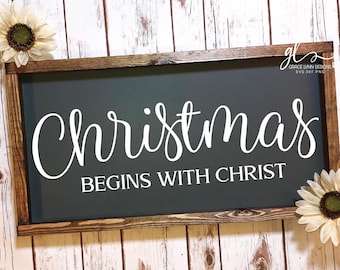 May include: A wooden sign with a dark gray background and white text that reads "Christmas Begins With Christ".