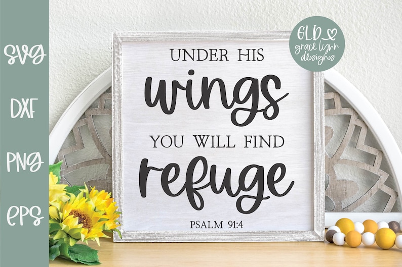 May include: A white wooden sign with black text that reads "Under His Wings You Will Find Refuge" and "Psalm 91:4". The sign is sitting on a wooden table with a decorative plate and yellow flowers.
