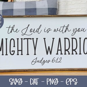 May include: A white wooden sign with the text "the Lord is with you MIGHTY WARRIOR Judges 6:12" in black lettering. The sign has a brown wooden frame.