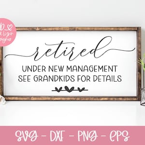 May include: A white sign with brown wood frame reads "retired" in cursive script, followed by "under new management see grandkids for details". Three small black hearts are below the text. The sign is on a white surface with a pink flower and a potted plant.